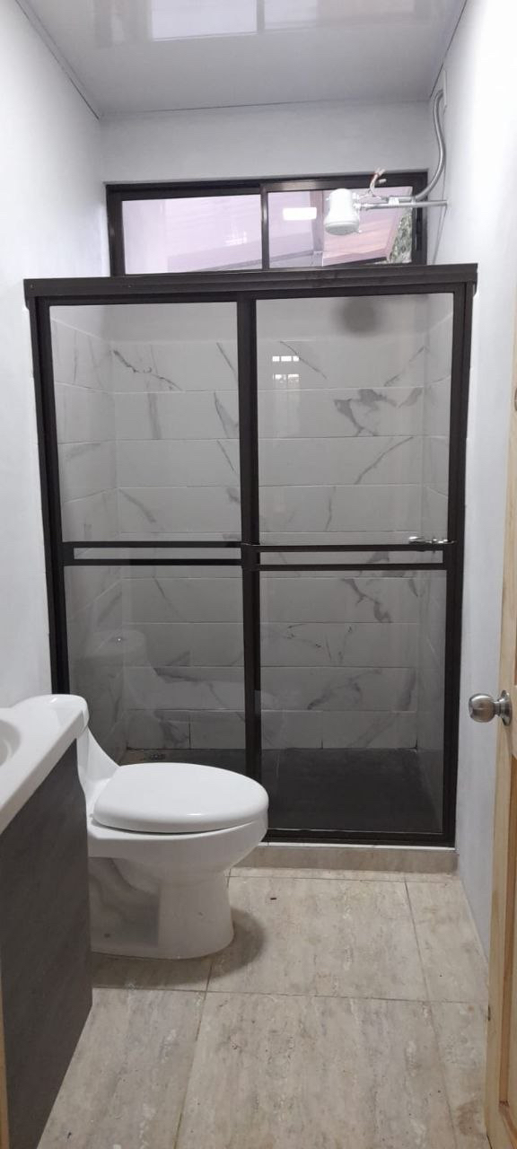 Baño interior terminado con azulejos blancos y ducha de vidrio templado